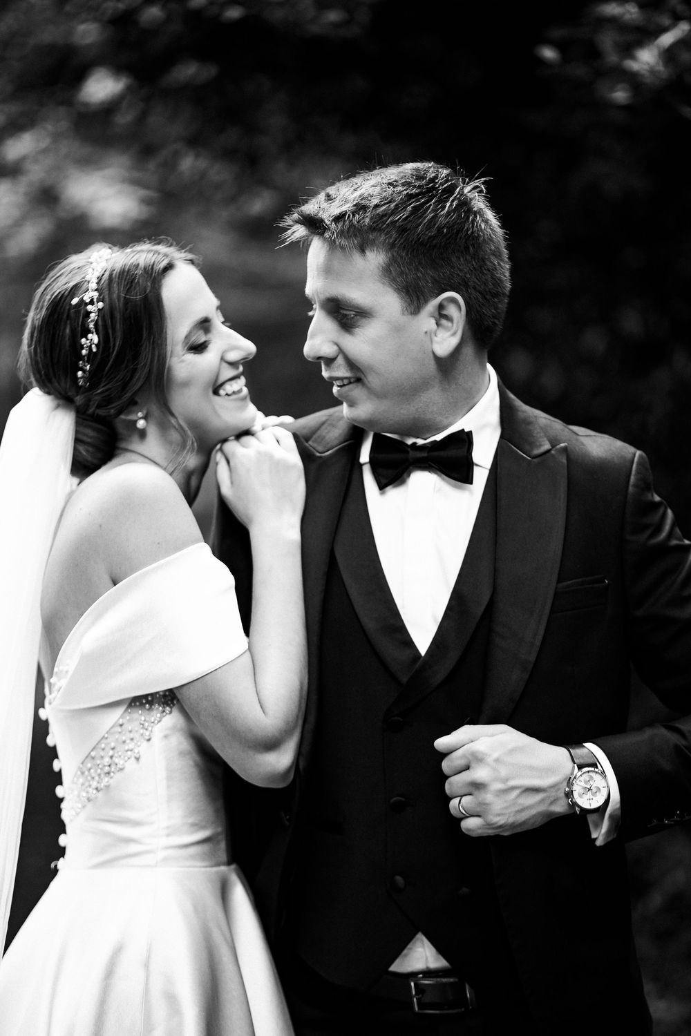 Black and white photo of smiling bride and groom in tuxedo sharing a romantic moment on their wedding day.
