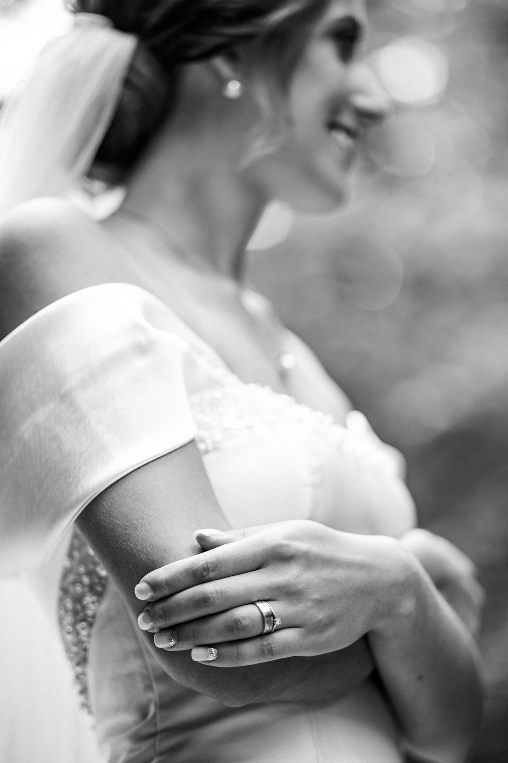Close-up black and white photo of a smiling bride in a lace gown with a wedding ring on her hand.