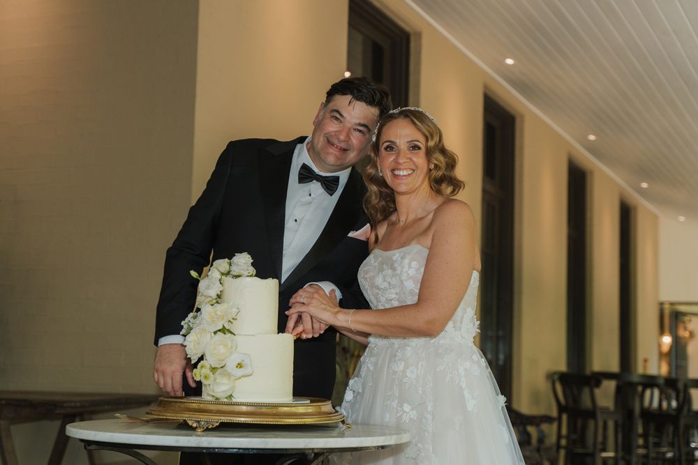 Bride and groom smiling together while cutting their elegant white wedding cake at their wedding reception sydney wedding photographer