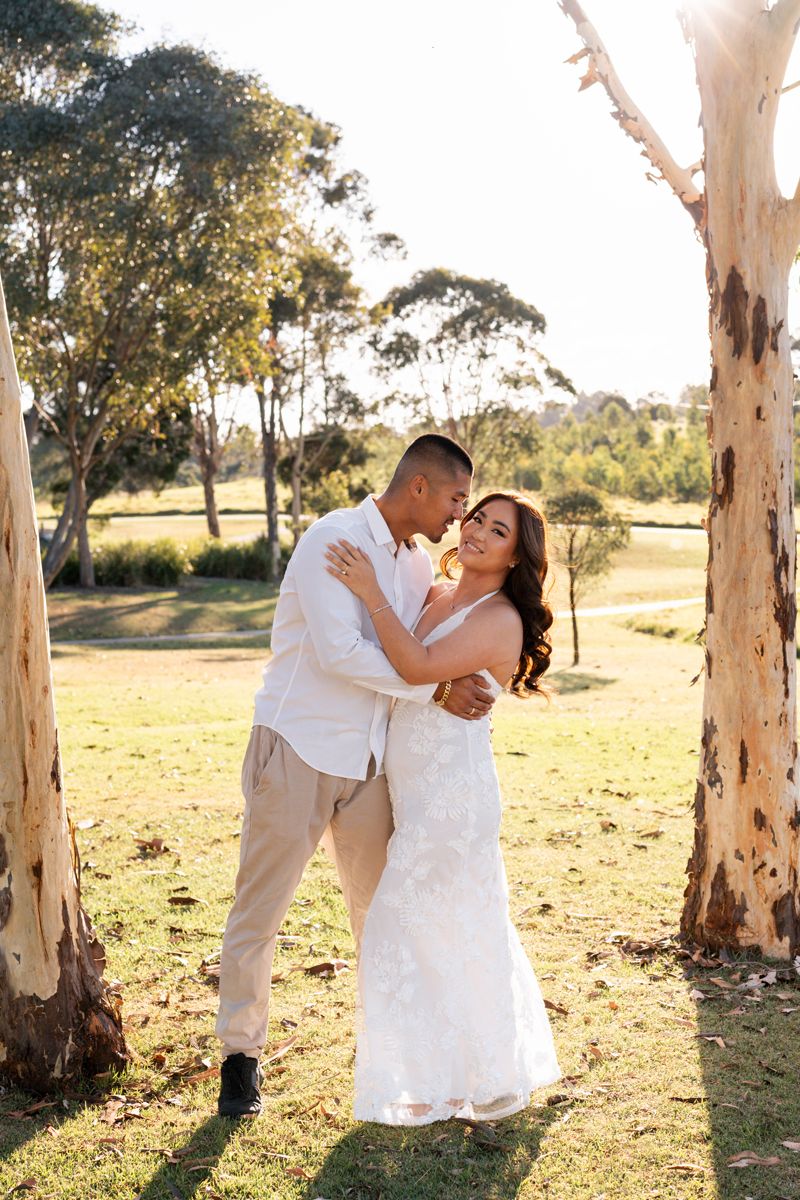 Couple outdoors between eucalyptus trees, bride in white gown and groom in beige suit, golden hour light elopement photoshoot western sydney