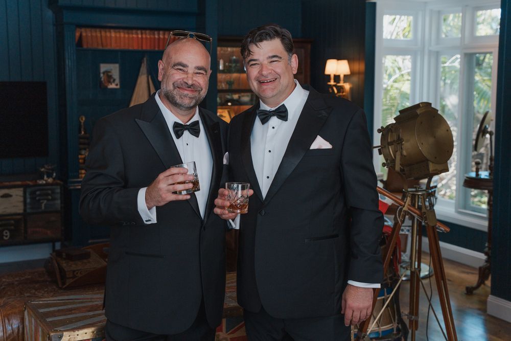 Two men in black tuxedos toasting with drinks at a formal event in an elegant room wedding photography rouse hill