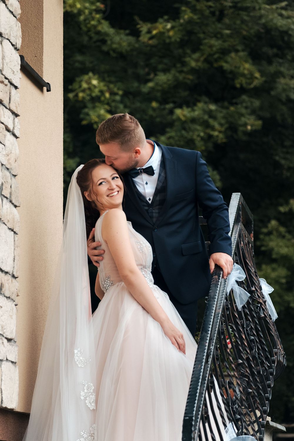 A groom in a navy suit kisses his smiling bride in a white gown and veil on an outdoor staircase in hunter valley