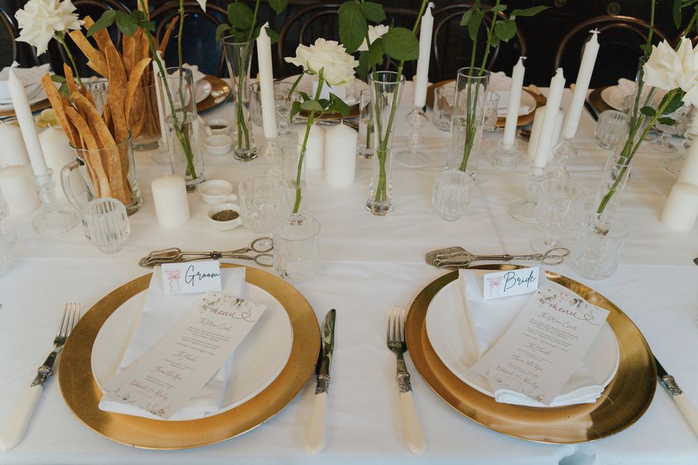 wedding table setting with gold charger plates, white menus, candles, and floral arrangements in glass vases wedding photographer rouse hill