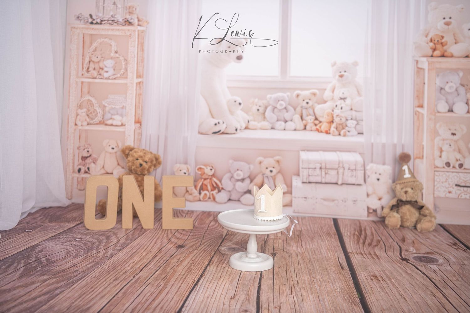 First birthday cake smash setup with teddy bears, white furniture, wooden floor, and ONE letters in a soft, neutral-toned studio.