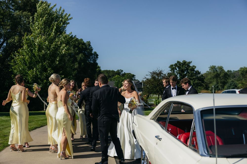 Wedding party in elegant attire gathering near a classic white vintage car on a sunny day outdoors at Wisconsin venue
