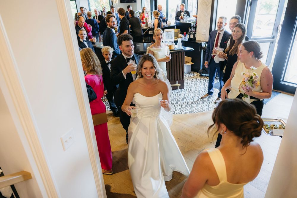 Bride in white gown smiling at wedding reception with guests and bridesmaid in yellow dress captured by candid photographer in Wisconsin