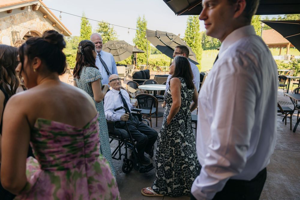 Wedding guests mingle outdoors, including an elderly man seated in a wheelchair at a reception captured by candid photographer in Wisconsin