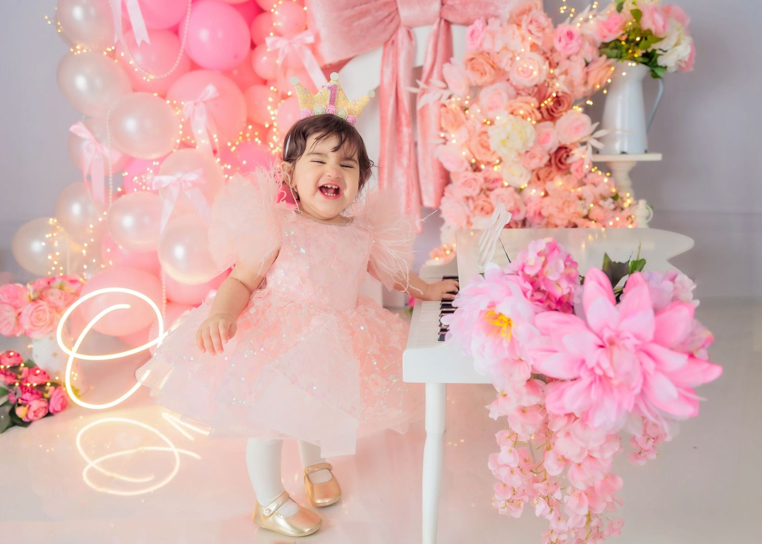Baby girl in pink dress at first birthday party with daisy balloons, bee decorations, and floral arrangement.