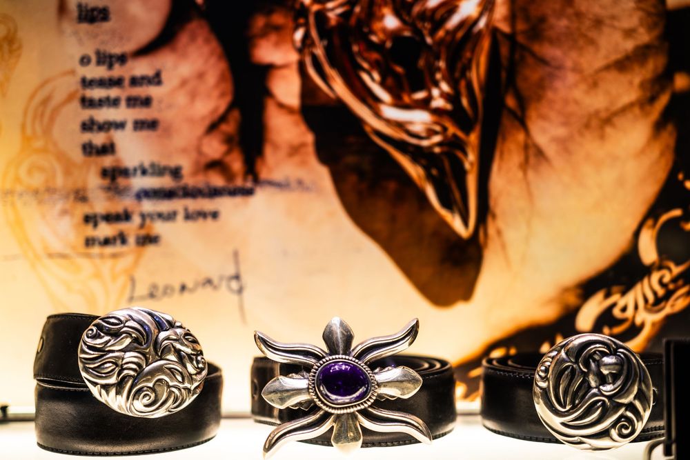 Three ornate silver belt buckles with black leather belts displayed against a decorative golden background.