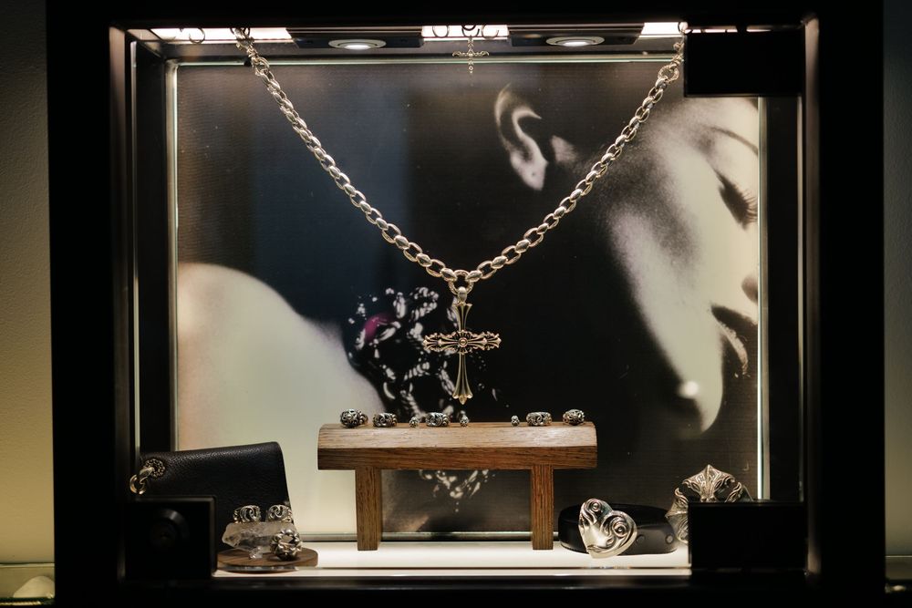 Luxury jewelry display case featuring a silver chain necklace with cross pendant and rings on a wooden stand.
