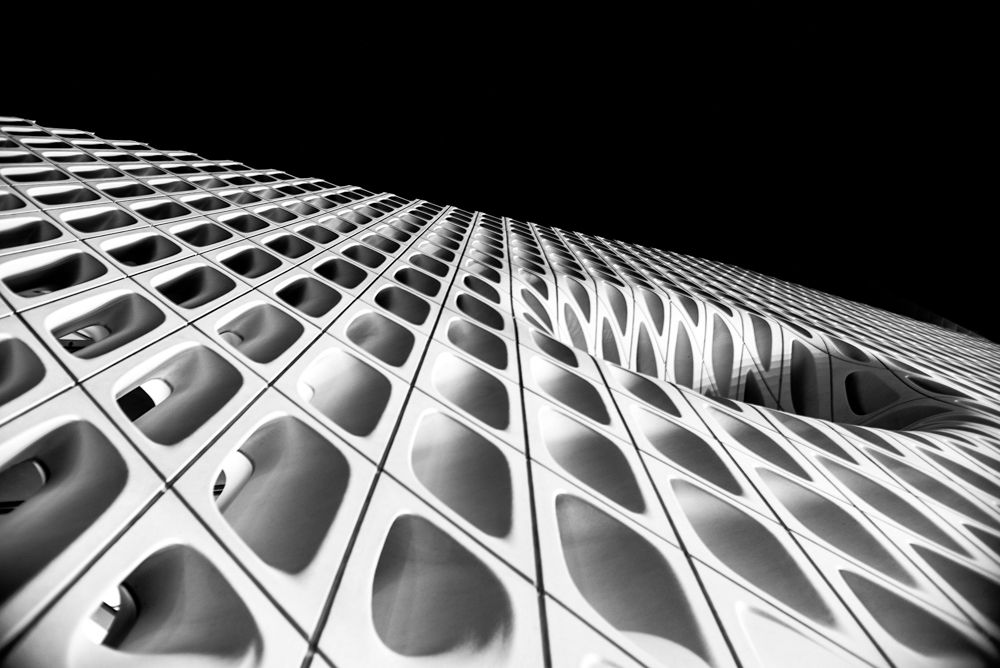 Black and white architectural photo of a modern building facade with geometric honeycomb pattern against dark sky.