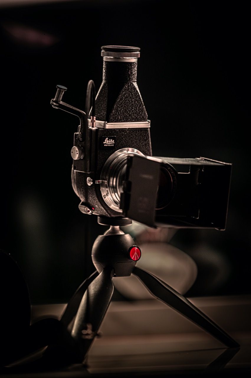 A vintage Leica camera mounted on a small tripod, dramatically lit against a dark background.