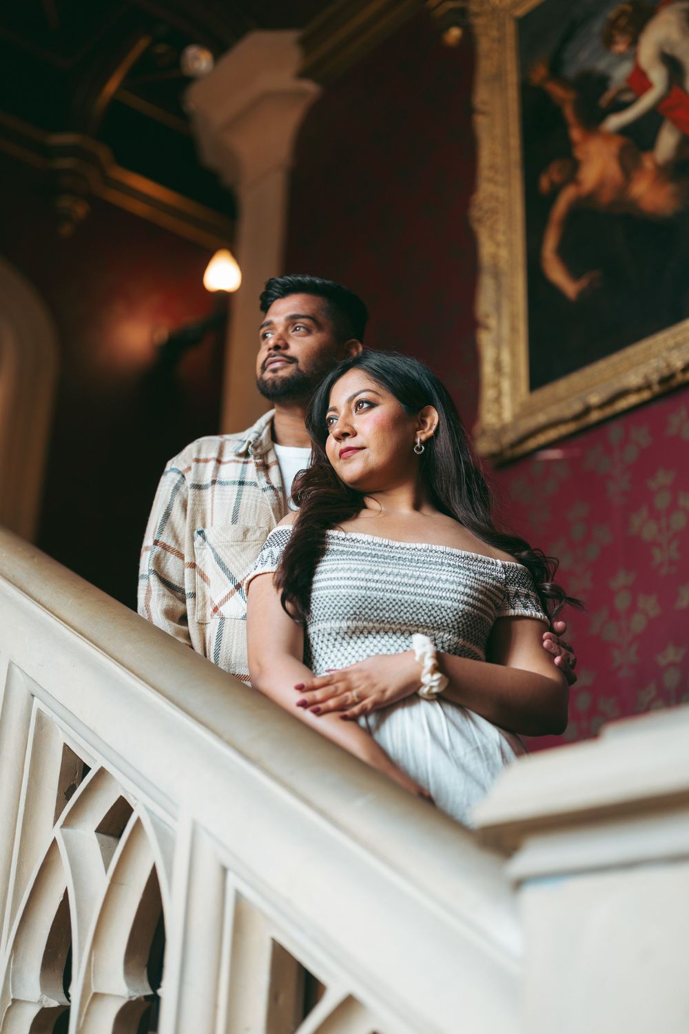Couple posing on grand staircase in elegant venue with ornate paintings.