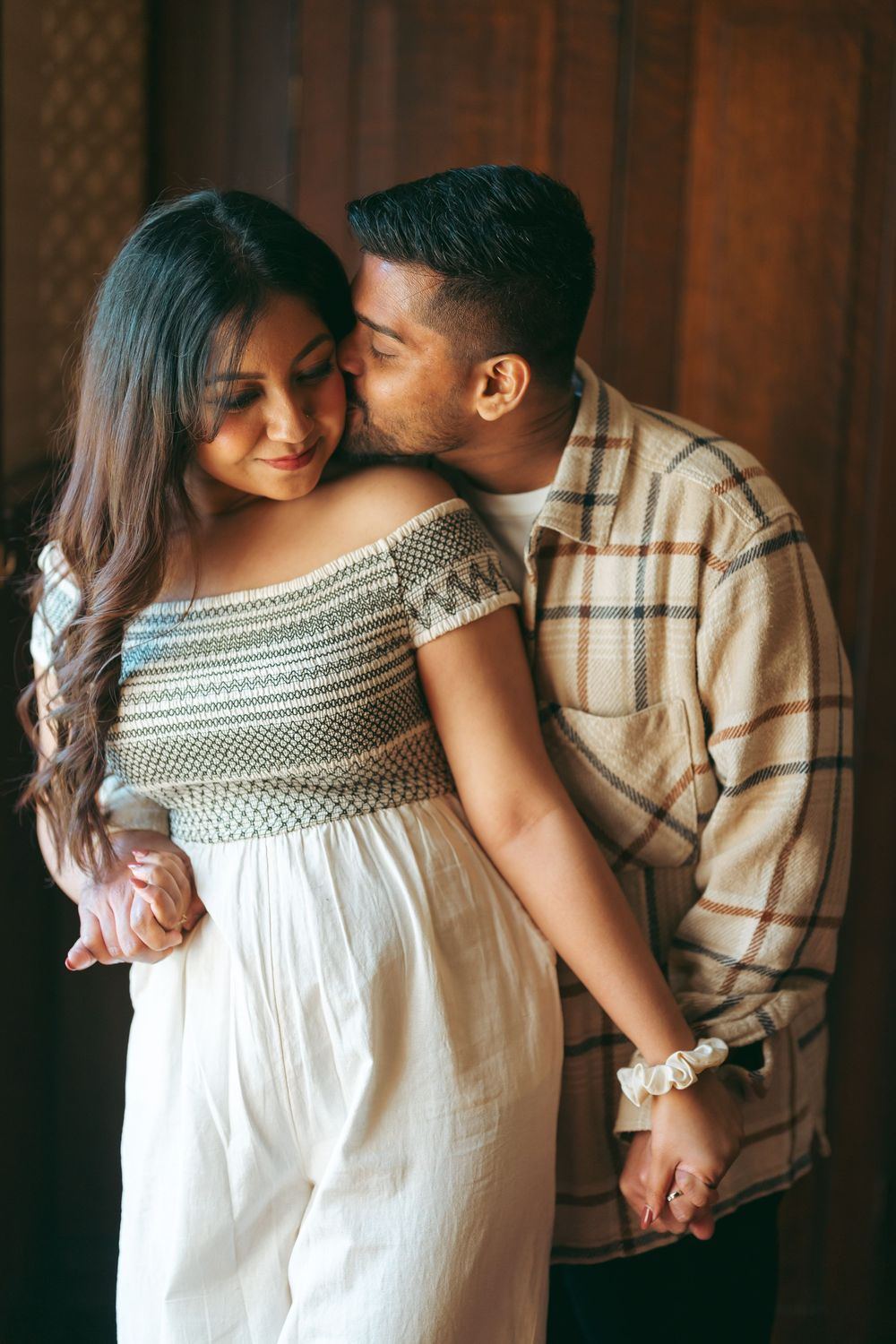 Man kissing woman on cheek while holding hands in warm indoor setting.