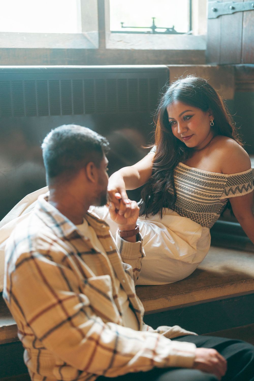 A couple sits together on a wooden bench, holding hands and sharing a tender moment in warm natural light.