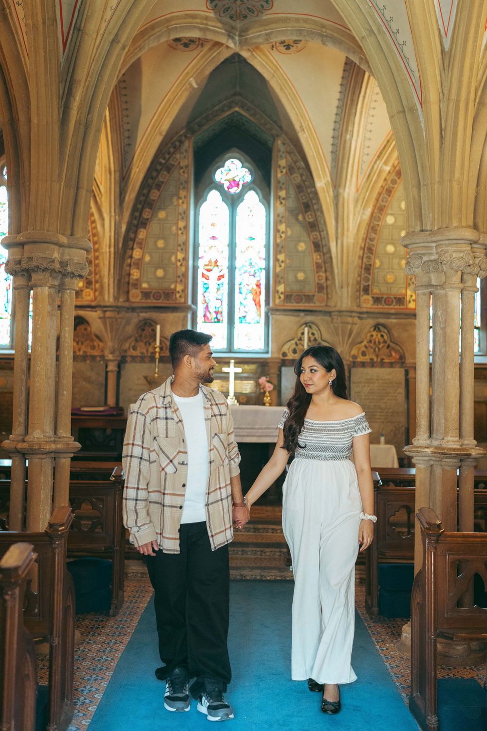 Couple holding hands in a stunning Gothic church with stained glass windows and ornate arched ceilings.
