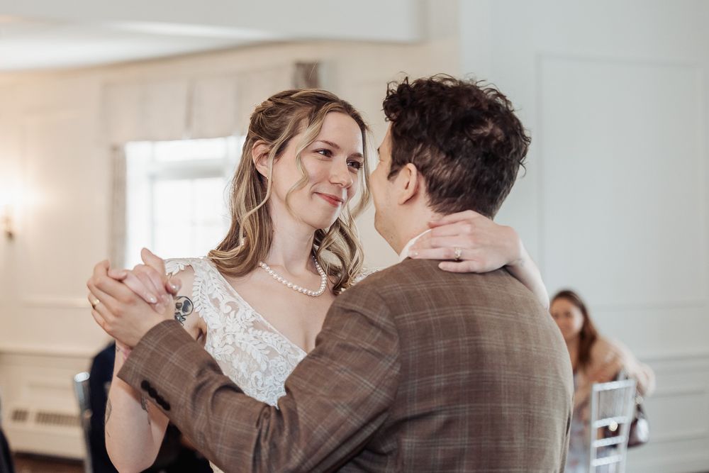 Bride and groom share their first dance, smiling lovingly at each other in a bright elegant venue.