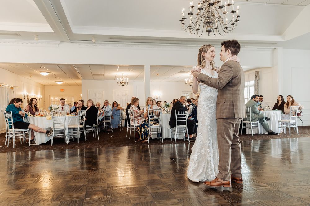 Bride and groom share their first dance in an elegant ballroom while wedding guests watch from decorated tables.