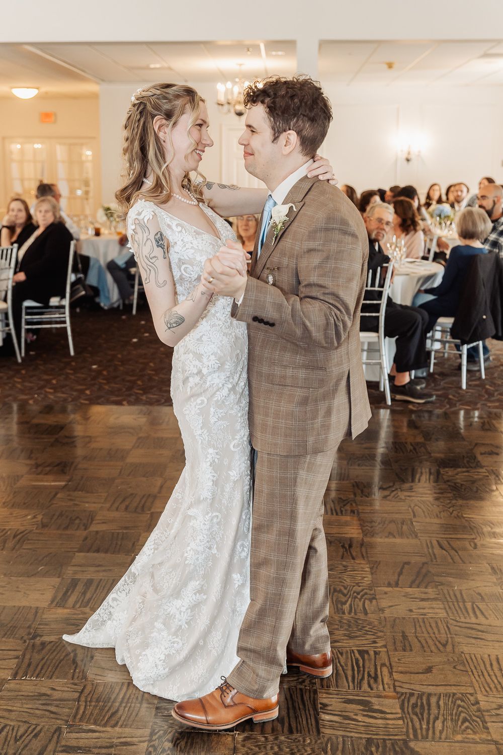 Bride and groom share their first dance in a elegant wedding reception hall with guests seated in the background.