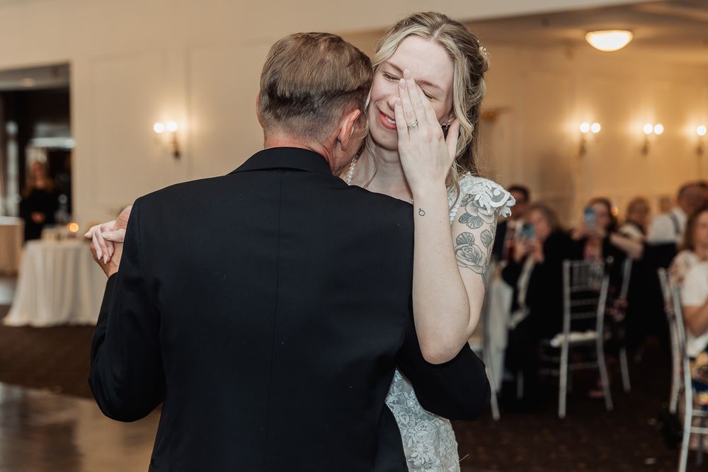 Emotional bride wiping tears during father-daughter dance at wedding.