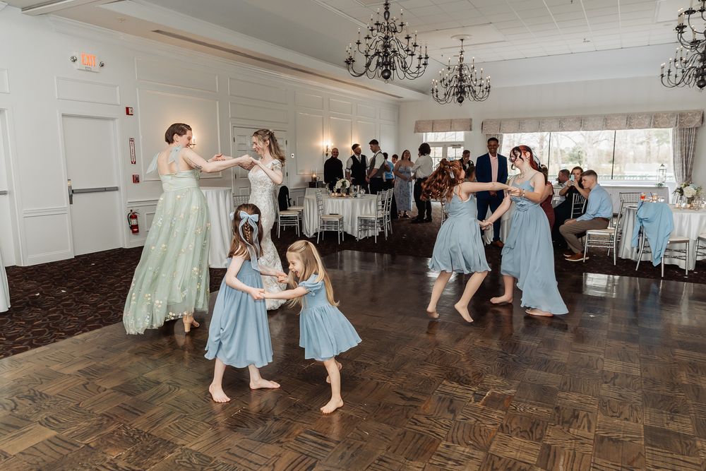 Bridesmaids and flower girls dance joyfully on wedding reception dance floor.