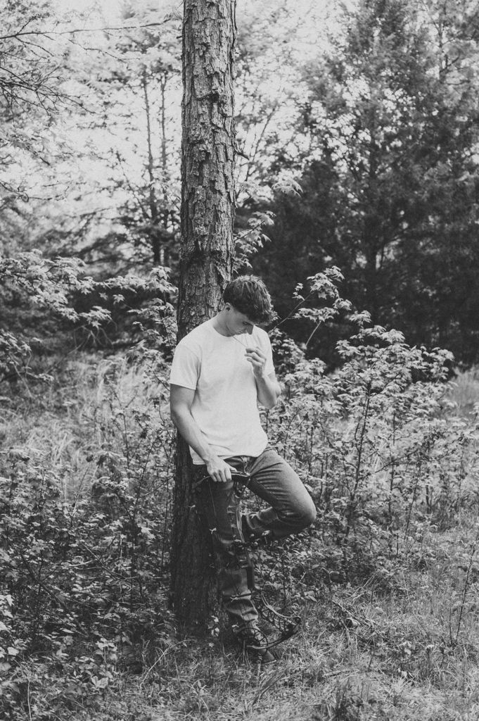 Young man leaning against a tree in a forest in black and white photo.