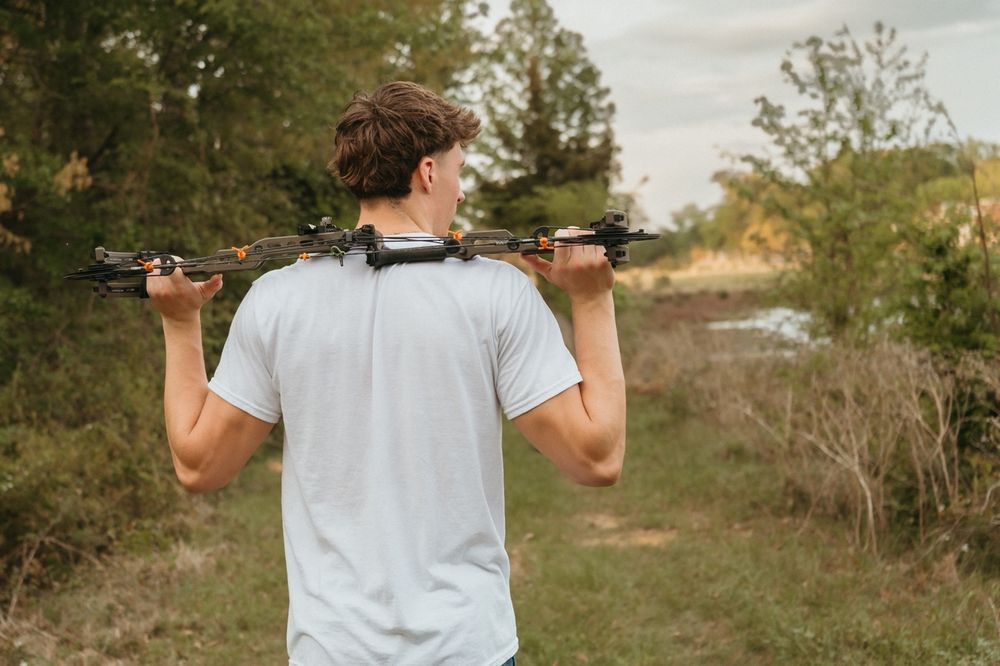 Young man carrying drone across shoulders walking on rural path through green vegetation.