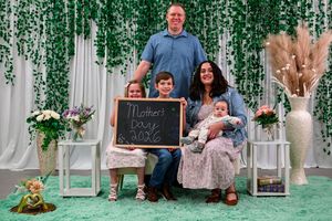 Family of five posing for a Mother's Day 2026 photo in front of a floral backdrop with greenery.