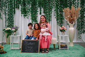A mother poses with three young children on Mother's Day 2026 against a green floral backdrop.