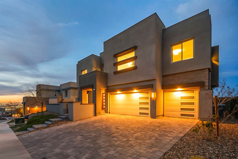 Modern two-story home with large garage doors, paver driveway, and warm lighting at twilight.
