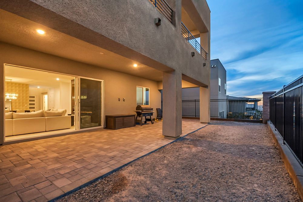 Spacious paver patio with outdoor seating and glass doors leading to a brightly lit interior at dusk.