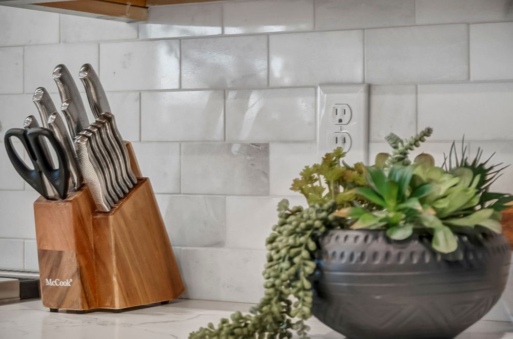 Kitchen detail showing a wooden knife block set and succulent plant arrangement against a white tile backsplash.
