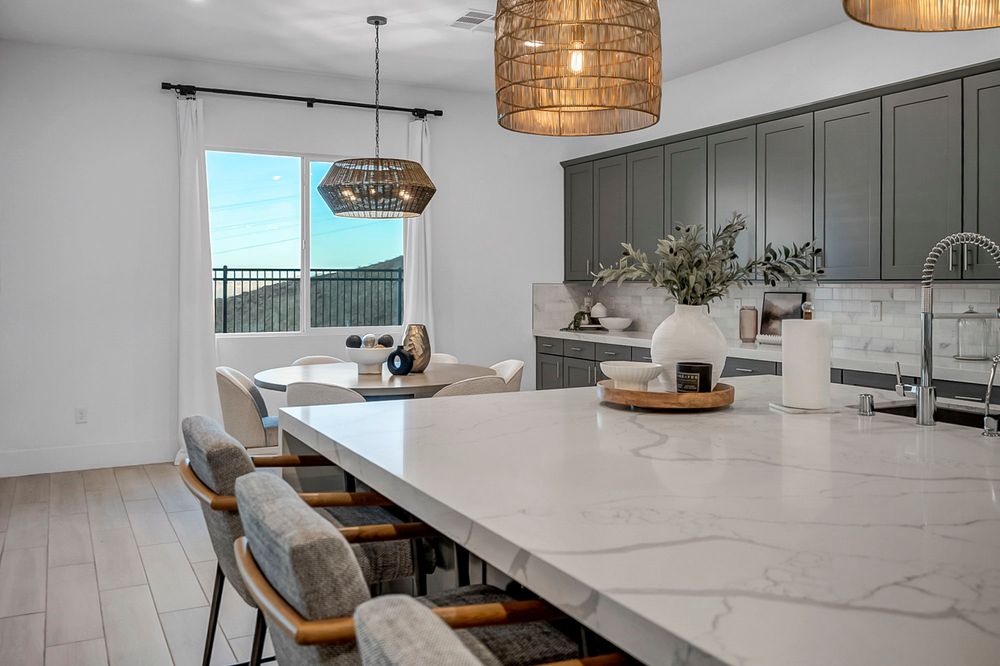 Open dining area with white quartz waterfall island, gray cabinetry, woven pendant lights, and mountain views.