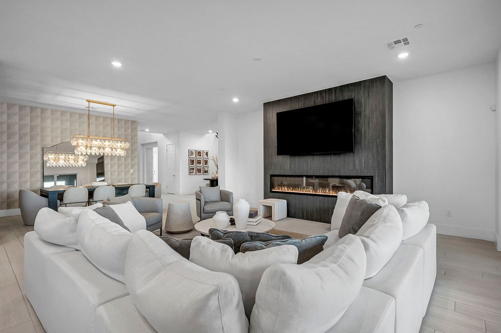 Spacious living room with white sectional sofas, linear fireplace, wall-mounted TV, and decorative wall panels.