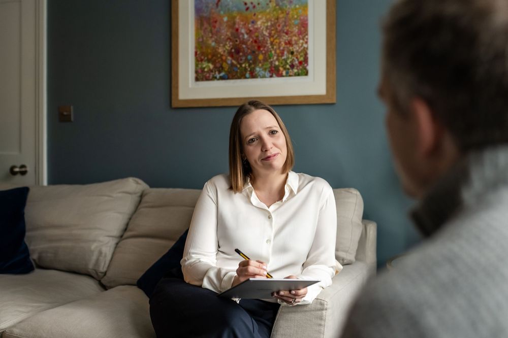 Woman therapist taking notes while listening attentively to a patient during a counseling session indoors.