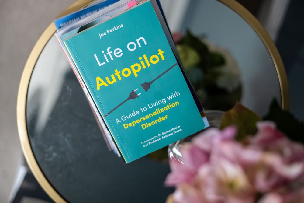 Book 'Life on Autopilot: A Guide to Living with Depersonalization Disorder' by Jon Perkins on a glass table.