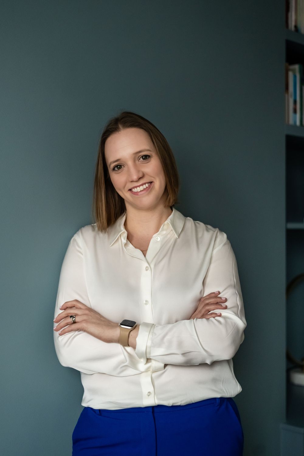 Psychologist in white blouse smiling with arms crossed against teal wall during a personal branding photo shoot