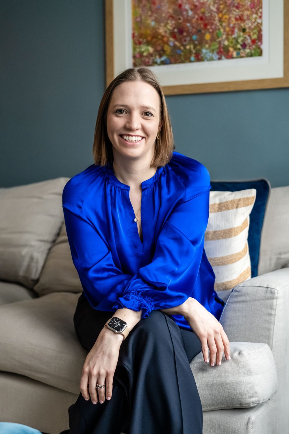 Smiling psychologist in blue satin blouse seated on gray sofa during a personal branding photoshoot