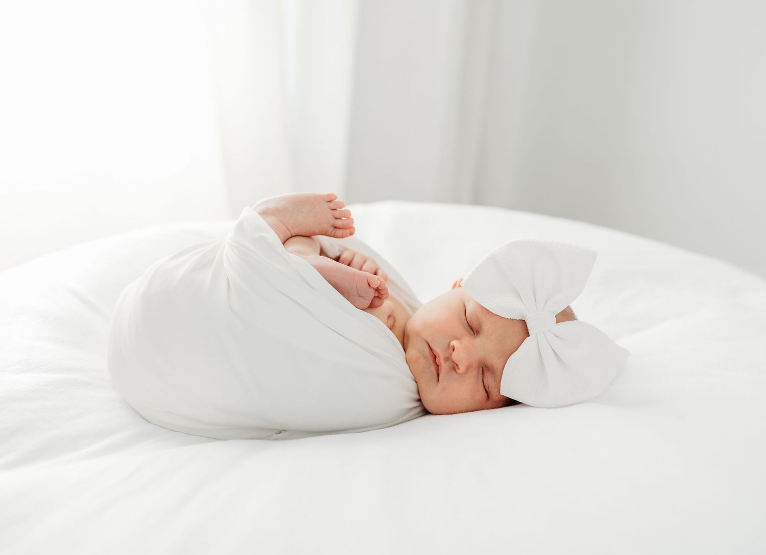 Adorable baby in white outfit and bow headband sleeps peacefully on a bright white bed.
simple timeless natural