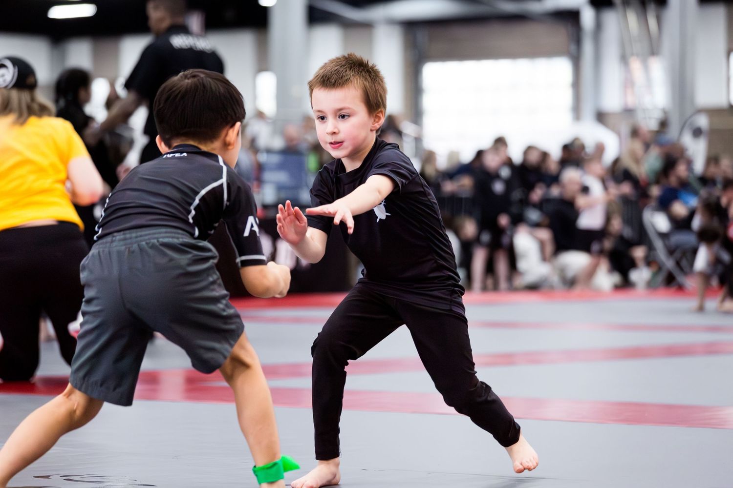 Martial artists perform dynamic kicks and strikes during a competitive sparring match on red training mats.