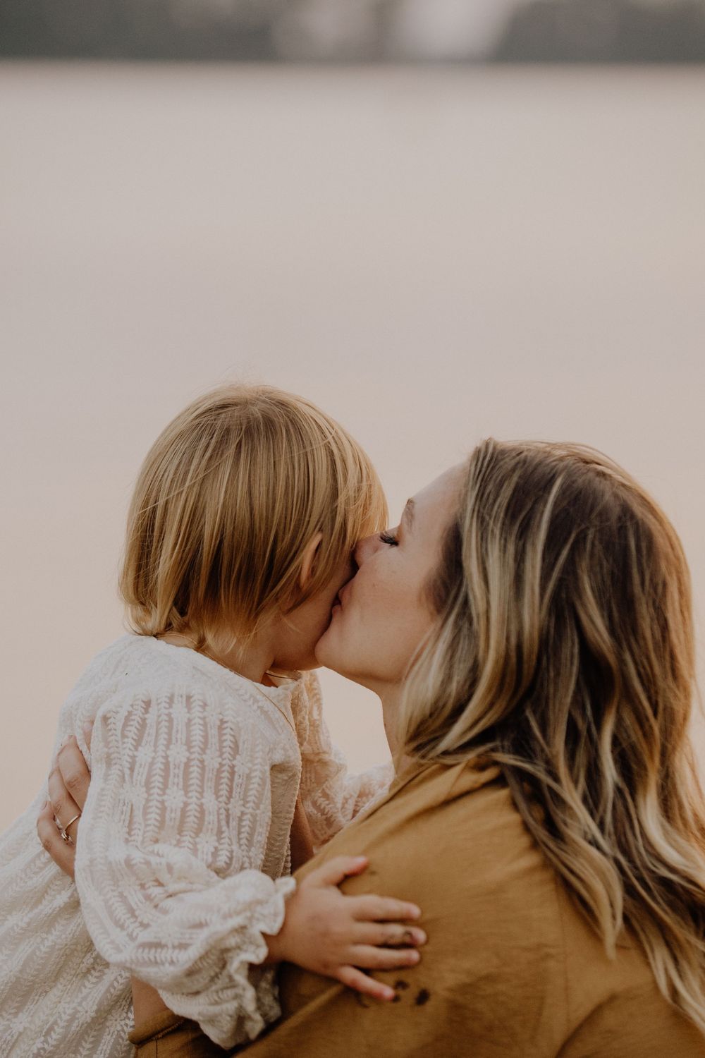 A tender moment between parent and child sharing a kiss while wearing cozy sweaters in warm natural lighting.