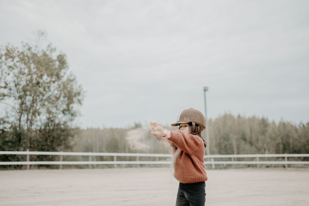 Someone wearing brown jacket dances alone in an outdoor arena on overcast day with white fence in background.