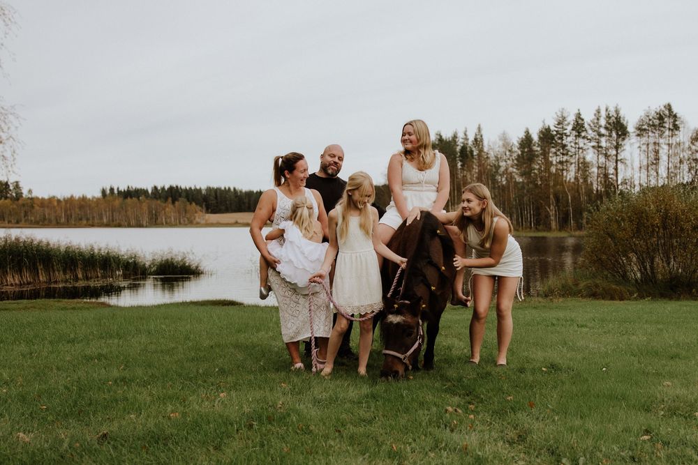 A group poses together on grassy fields near a lake during sunset in matching white outfits.