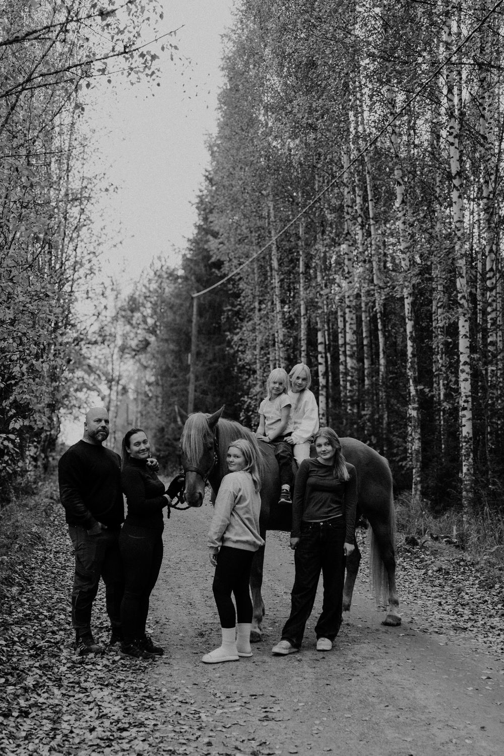 A group of people walking together on a tree-lined path through a forest in black and white vintage photography.