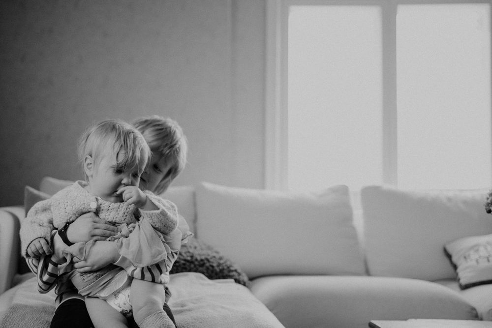 Two children share a sweet moment together on a couch in black and white.