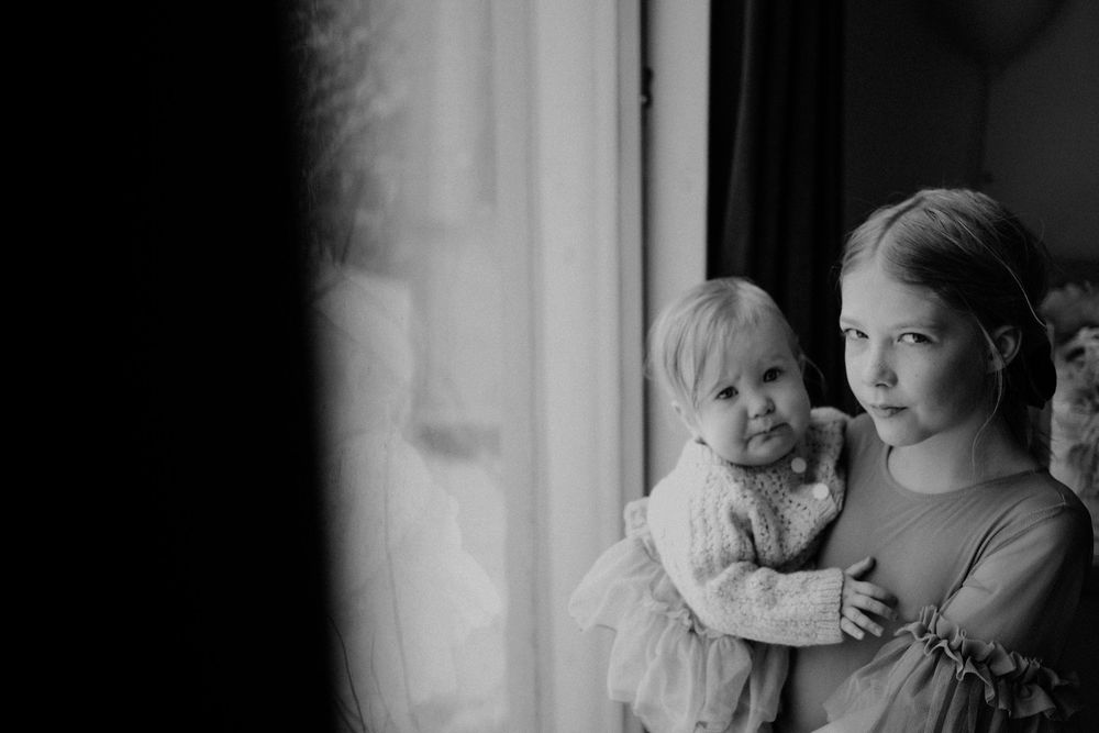 A black and white photograph shows a mother and small child gazing through a window in soft natural light.