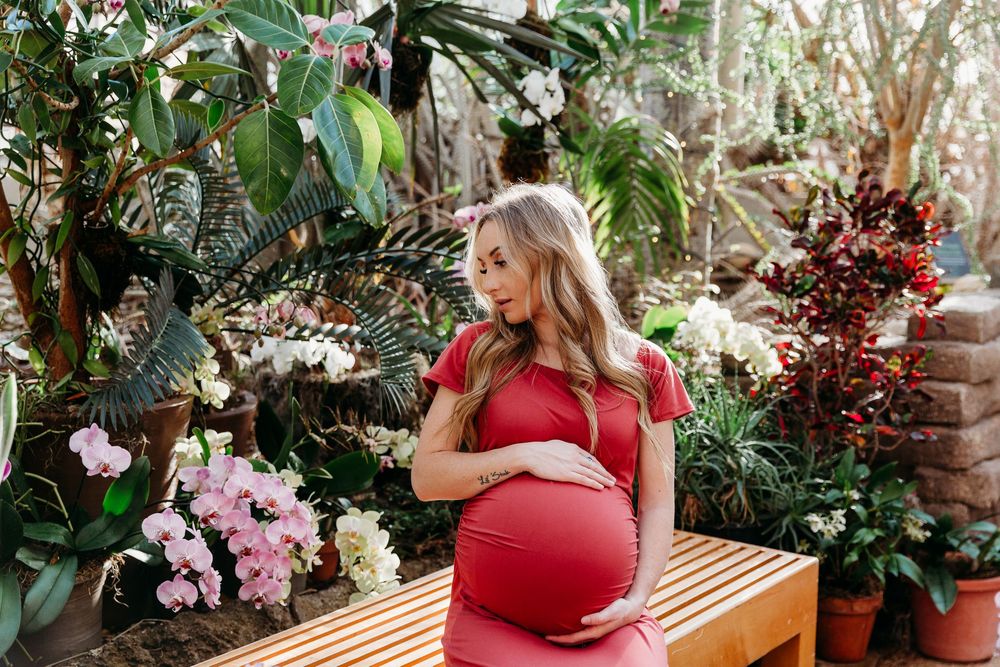 Maternity portrait in a botanical garden with woman in red dress among pink orchids.