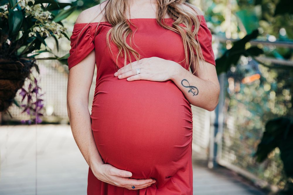 Close-up maternity photo showing hands cradling baby bump in red off-shoulder dress.