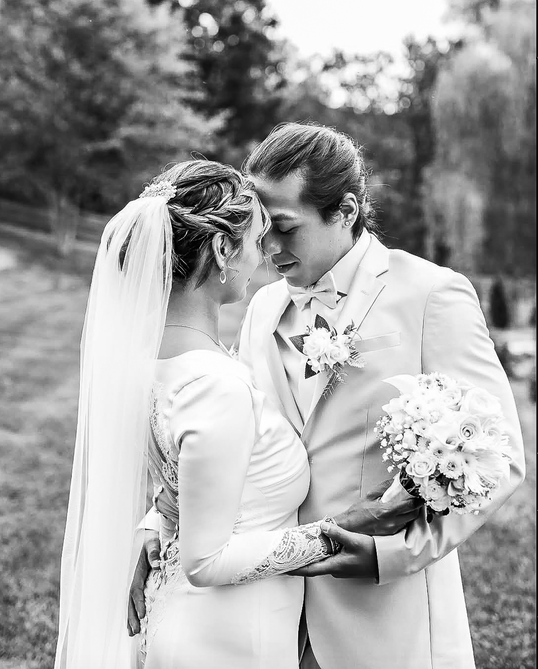 Romantic black and white wedding portrait with couple embracing outdoors holding a floral bouquet.