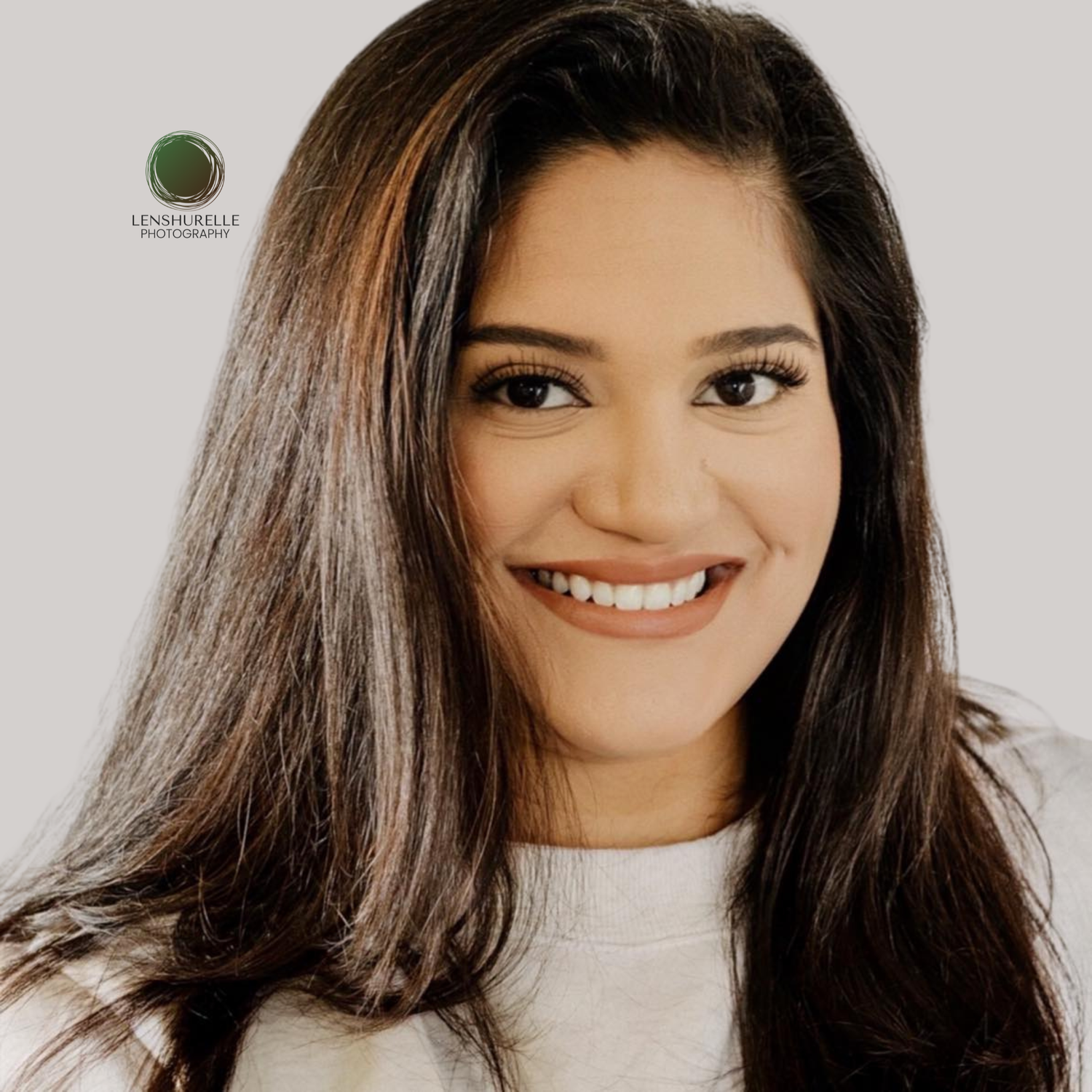 Professional headshot of smiling young woman with long brown hair against white background.